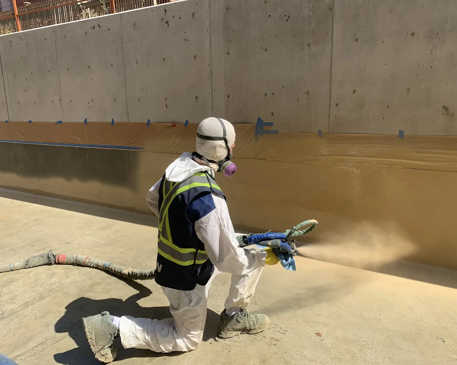 Applicator in a white suit and respirator spraying a coating across a concrete floor